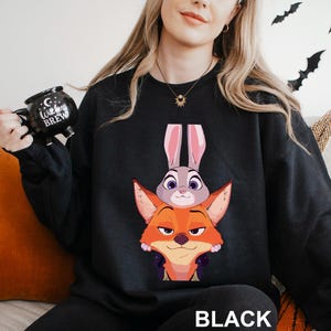May include: Black sweatshirt featuring a cartoon image of a fox and a bunny. The fox is orange and the bunny is gray with pink ears. The word "BLACK" is printed in white at the bottom of the sweatshirt.