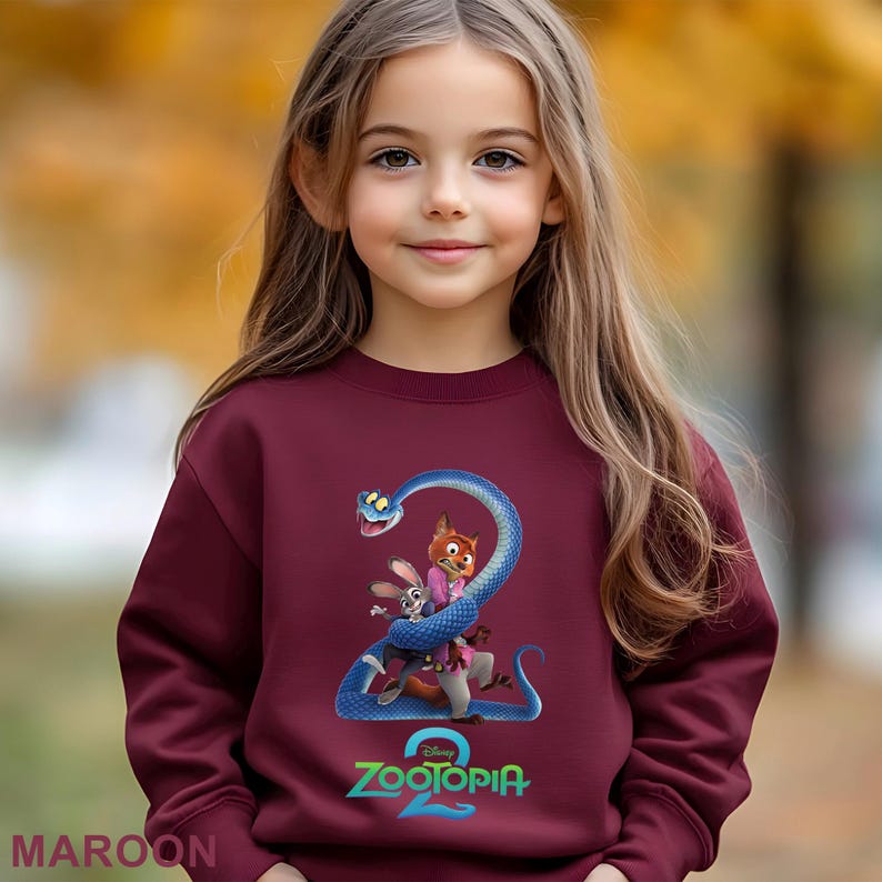 May include: Maroon sweatshirt featuring a colorful graphic from the movie Zootopia 2. The design includes a blue snake, a fox, and a rabbit. The word "Zootopia" is written in green and white. The word "MAROON" is written in white at the bottom left.
