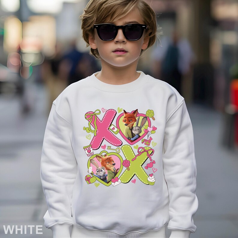 May include: White sweatshirt featuring a colorful graphic of the characters Nick Wilde and Judy Hopps from Zootopia, with the letters "XO" and heart shapes. The sweatshirt is worn by a child wearing sunglasses.