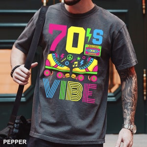 May include: A dark gray t-shirt with a colorful graphic design featuring the text "70's VIBE" and a pair of roller skates with a cassette tape.