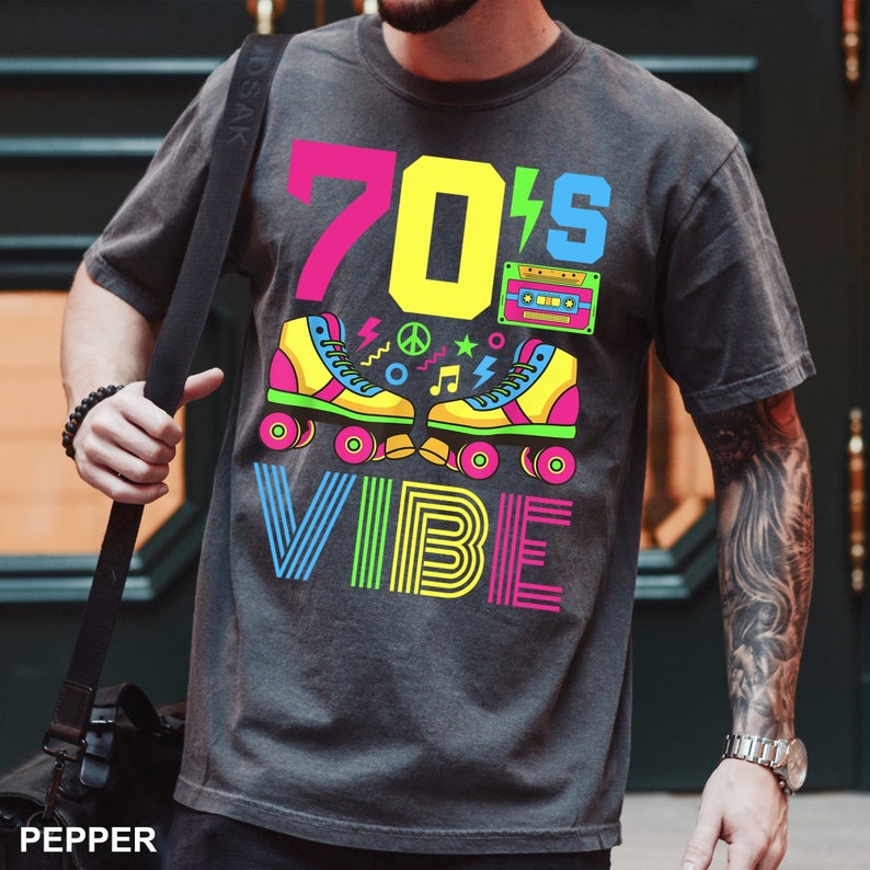 May include: A dark gray t-shirt with a colorful graphic design featuring the text "70's VIBE" and a pair of roller skates with a cassette tape.