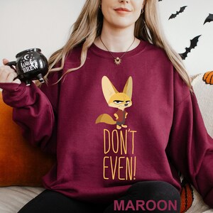 May include: Maroon sweatshirt with a cartoon fennec fox and the text "DON'T EVEN!". The fox wears a red vest. The sweatshirt is a solid maroon colour. The word "MAROON" is printed at the bottom of the sweatshirt.
