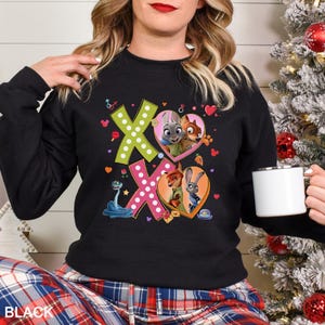 May include: Black sweatshirt with a colorful graphic featuring the characters from Zootopia, including Judy Hopps and Nick Wilde, inside heart shapes. The design includes the letters "XO" and other decorative elements. The word "BLACK" is printed at the bottom.