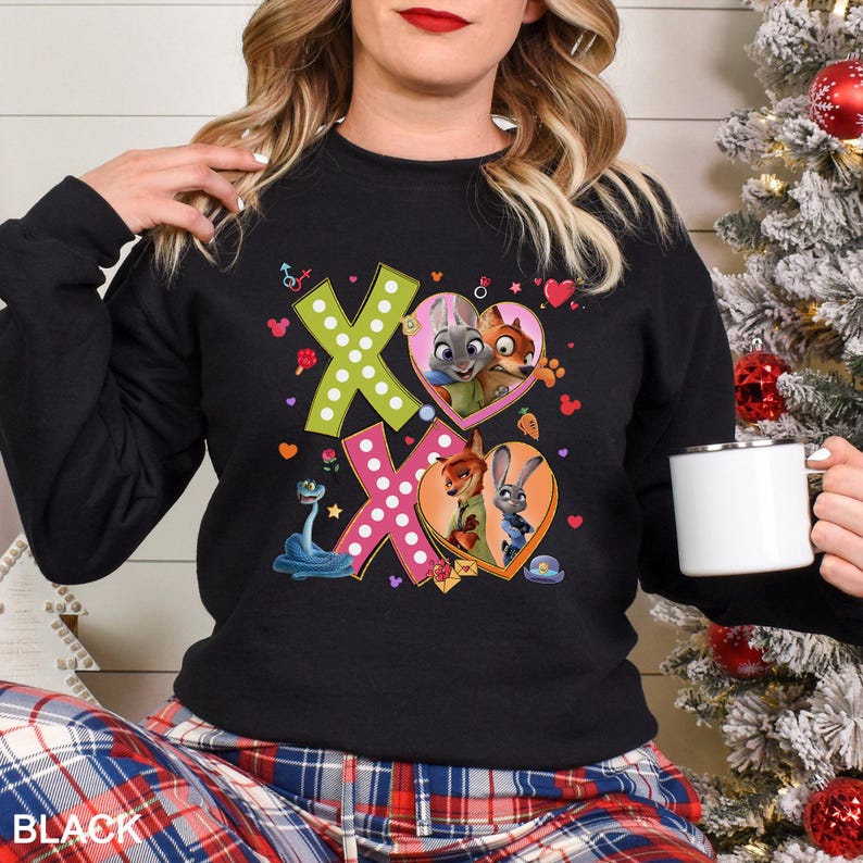 May include: Black sweatshirt with a colorful graphic featuring the characters from Zootopia, including Judy Hopps and Nick Wilde, inside heart shapes. The design includes the letters "XO" and other decorative elements. The word "BLACK" is printed at the bottom.