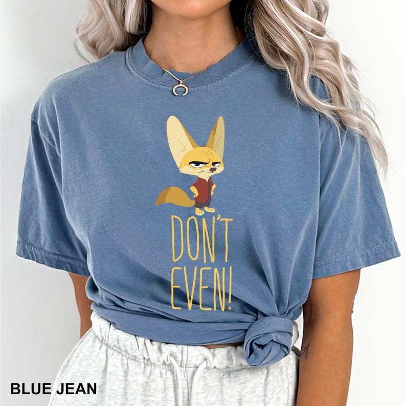 May include: Blue jean-colored t-shirt featuring a cartoon fox character with an angry expression. The shirt has the text "DON'T EVEN!" in yellow. The shirt is a short-sleeved, crew neck style.