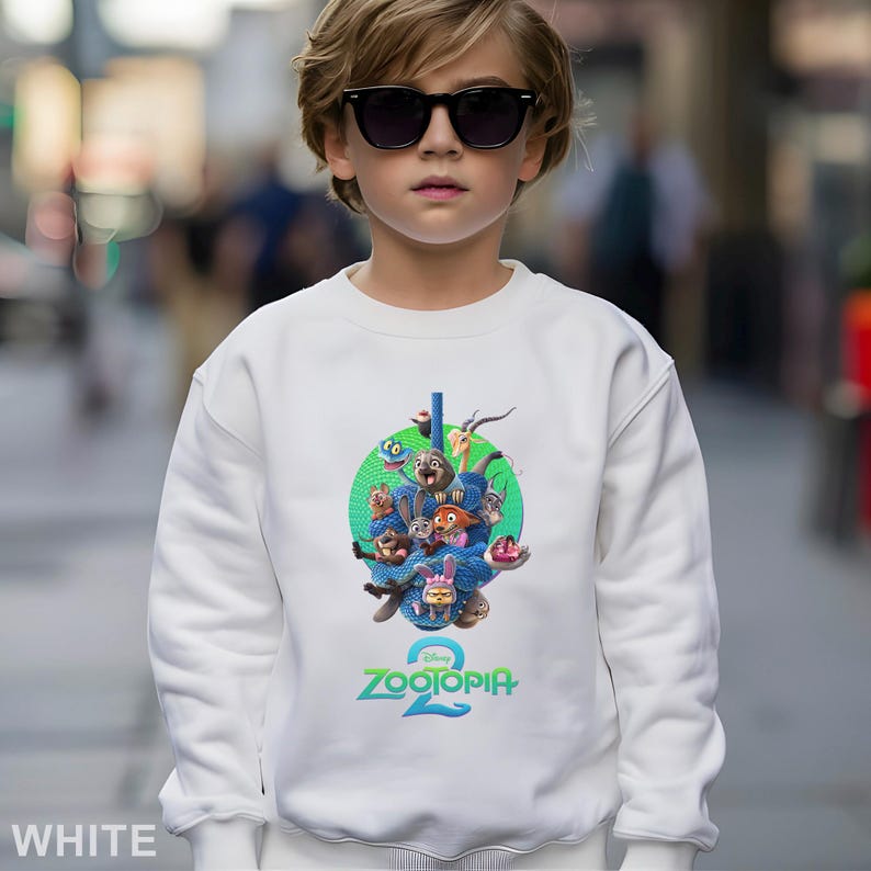 May include: White sweatshirt featuring a colorful graphic of characters from the Disney movie "Zootopia 2". The graphic is set against a green circle and includes the movie's title in blue and green. The sweatshirt is a crew neck style.