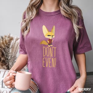 May include: Berry-colored t-shirt featuring a cartoon fox with an angry expression. The fox is wearing a red vest. Below the fox is the text "DON'T EVEN!" in yellow. The shirt is a crew neck style.