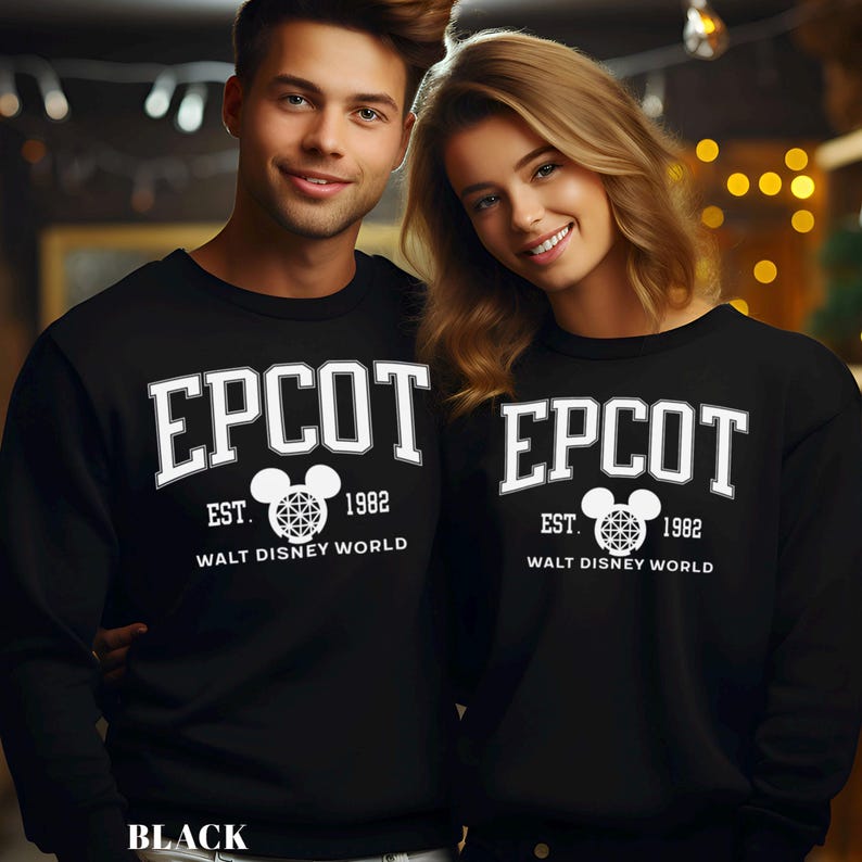 K&ouml;nnte beinhalten: Schwarze Sweatshirts mit dem Wort "EPCOT" in wei&szlig;er Schrift im College-Stil. Darunter steht der Text "EST. 1982 WALT DISNEY WORLD" in Wei&szlig;, mit einer Mickey-Mouse-Kopf-Grafik. Das Wort "BLACK" steht unten.