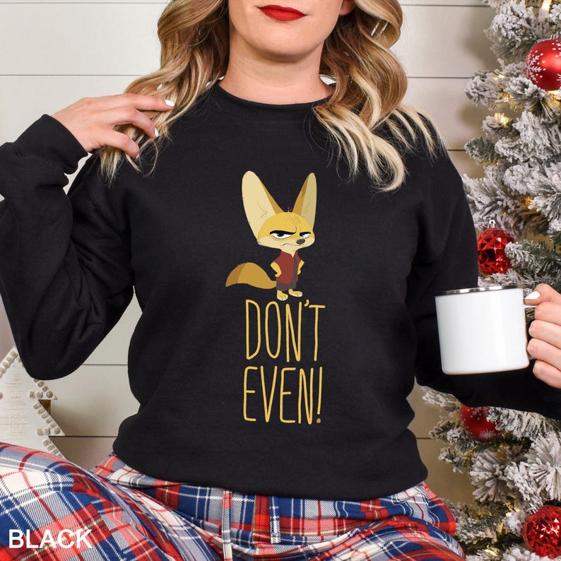 May include: Black sweatshirt with a cartoon fennec fox wearing a red vest. The text "DON'T EVEN!" is below the fox in yellow. The sweatshirt is worn with plaid trousers. The image also shows a white mug.
