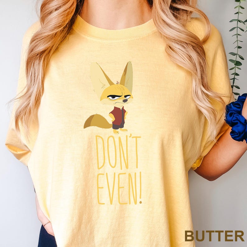 May include: Butter-colored t-shirt featuring a cartoon fennec fox with an annoyed expression, wearing a maroon vest and dark pants. The text "DON'T EVEN!" is printed below the fox in yellow. The word "BUTTER" is printed at the bottom right.