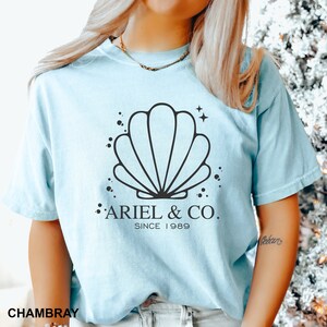 May include: A light blue t-shirt with a black seashell graphic and the text "Ariel & Co. Since 1989".