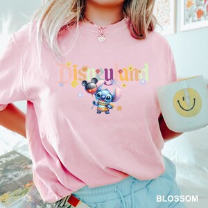 Puede incluir: Camiseta rosa con un gr&aacute;fico colorido de "Disneyland" que presenta a Stitch sosteniendo un globo de Mickey Mouse.