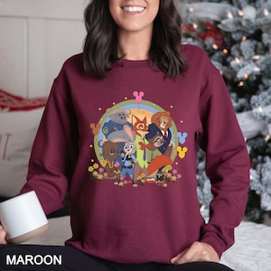 May include: Maroon sweatshirt with a cartoon animal character graphic. The design includes a rainbow, flowers, and Mickey Mouse-shaped balloons. The word "MAROON" is printed at the bottom of the sweatshirt.