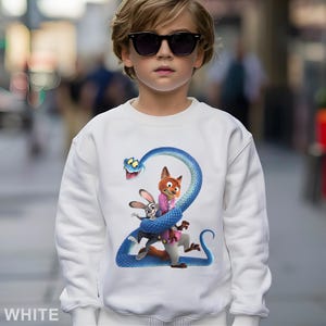 May include: White sweatshirt featuring a colorful graphic of characters from the movie Zootopia. The design includes a blue snake, a fox, and a rabbit. The word "WHITE" is printed at the bottom of the sweatshirt.