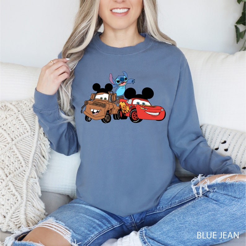 May include: A blue sweatshirt with a graphic of Stitch, Mater, and Lightning McQueen from Disney Pixar. The characters are wearing Mickey Mouse ears.