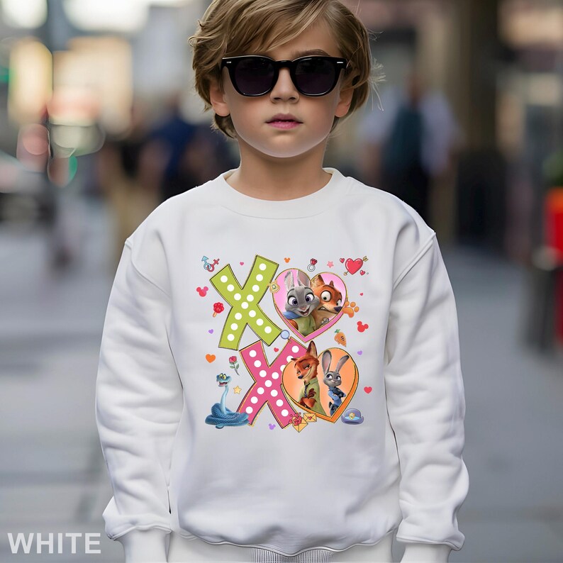 May include: White sweatshirt featuring a colorful graphic of the characters from the movie Zootopia. The design includes the letters "XO" with heart-shaped images of the characters. The word "WHITE" is printed at the bottom.