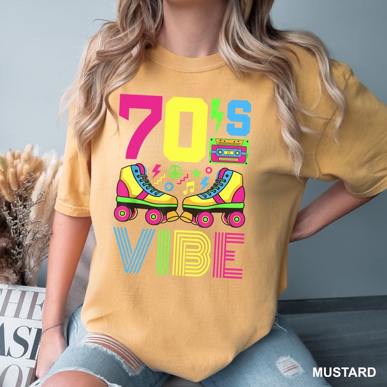 May include: A mustard yellow t-shirt with the text "70's VIBE" in rainbow colors. The design includes a retro cassette tape, peace sign, and roller skates.