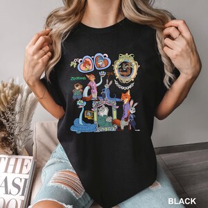 May include: Black t-shirt featuring colorful cartoon characters from the movie Zootopia. The design includes various characters in frames and a snake. The word "Zootopia" is printed in green.