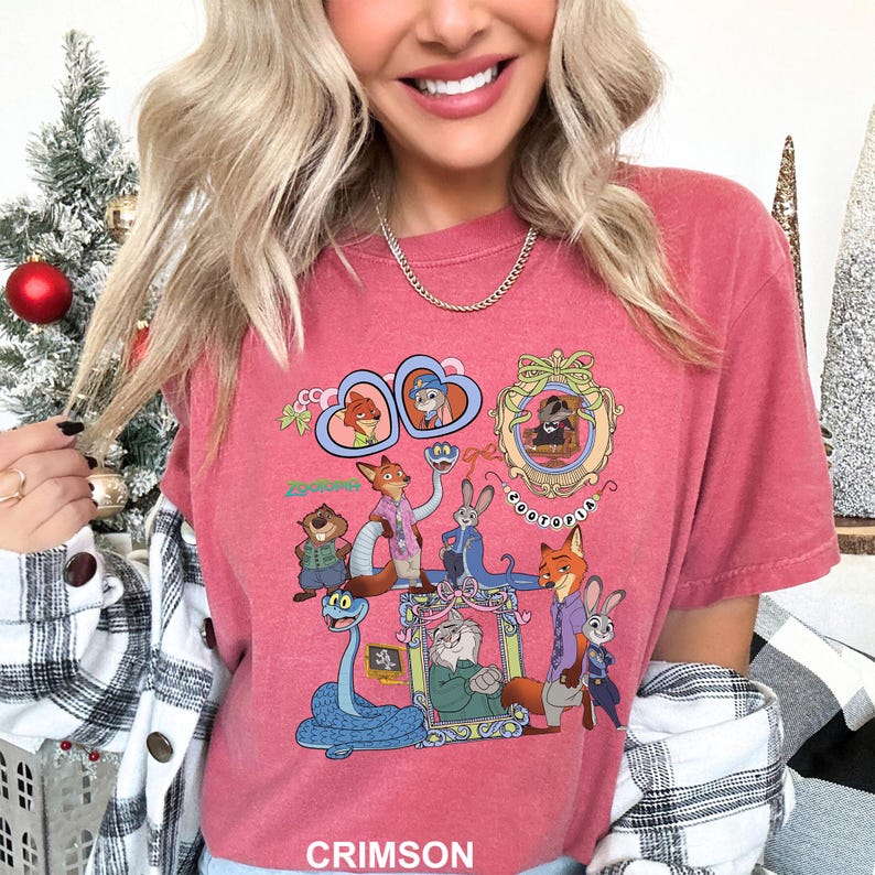 May include: Crimson-colored t-shirt featuring a colorful graphic of characters from Zootopia. The design includes framed portraits and various animal characters. The word "ZOOTOPIA" is also visible in the design.