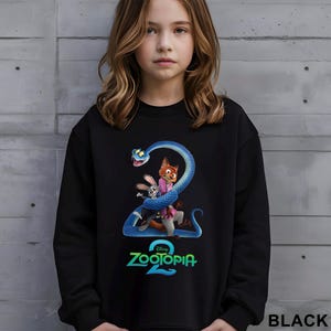 May include: Black sweatshirt featuring a colorful graphic from the movie Zootopia 2. The design includes a blue snake wrapped around the characters Nick Wilde, Judy Hopps, and others. The text "Zootopia 2" is displayed in green and blue.