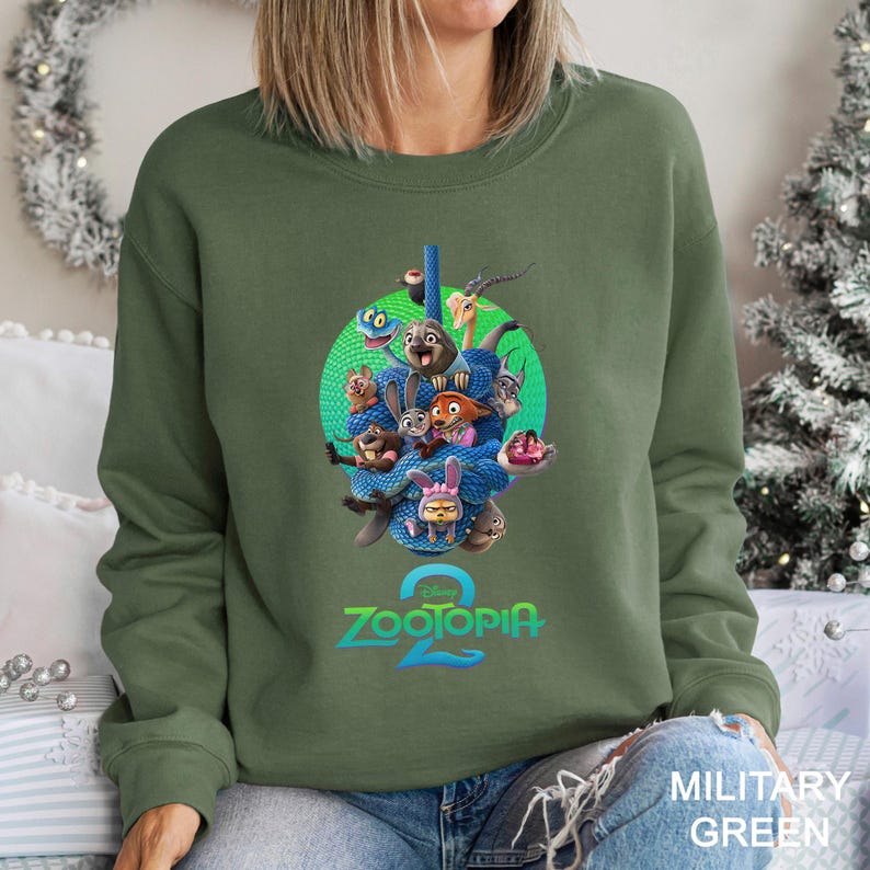 May include: Military green sweatshirt featuring a colorful graphic of characters from the animated film "Zootopia 2". The design includes a group of animal characters in a blue snake-like formation, with the film's title in blue and green.