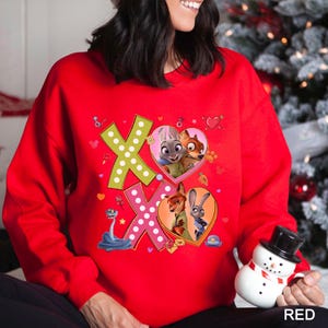 May include: A red sweatshirt featuring the characters from Zootopia. The design includes the letters "XO" with heart-shaped images of the characters. The sweatshirt is a vibrant red color, perfect for fans of the animated movie.