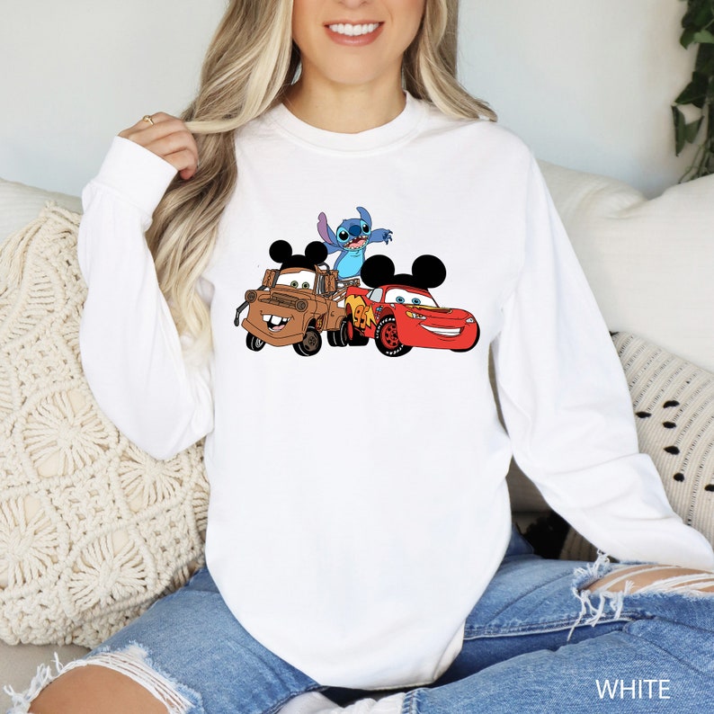 May include: White long-sleeved sweatshirt with a graphic print of Stitch, Mickey Mouse, and Mater from Disney's Cars. The characters are in a playful pose, with Stitch on top of Mater and Mickey Mouse driving a red race car.