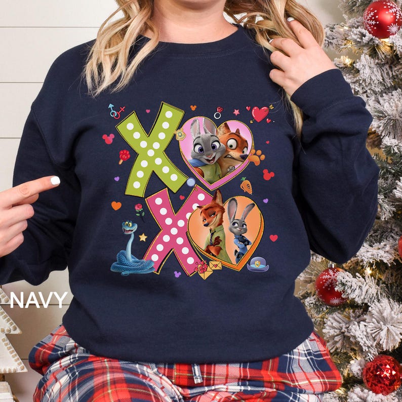 May include: Navy blue sweatshirt featuring the characters from Zootopia. The design includes the letters "XO" in green and pink, with heart-shaped illustrations of Judy Hopps, Nick Wilde, and other characters. The word "NAVY" is printed on the bottom left.