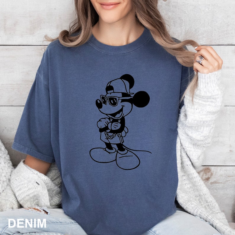 Może przedstawiać: Koszulka w ciemnoniebieskim kolorze z czarno-białym nadrukiem przedstawiającym Myszke Miki w okularach przeciwsłonecznych i czapce z daszkiem.