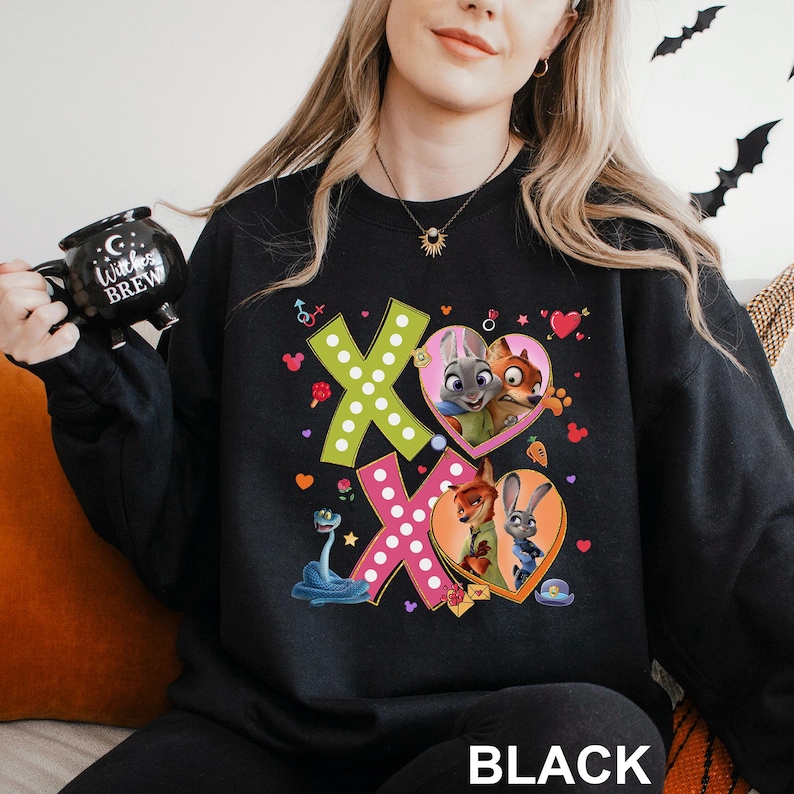 May include: Black sweatshirt featuring the word "BLACK" at the bottom. The design includes two "XO" shapes with polka dots, hearts, and cartoon characters from Zootopia. The characters are inside heart-shaped frames.