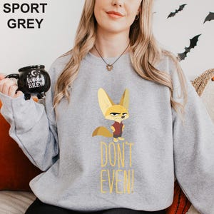 May include: Grey sweatshirt with a cartoon fox character and the text "DON'T EVEN!" in yellow. The fox wears a red shirt. The sweatshirt is a casual style.