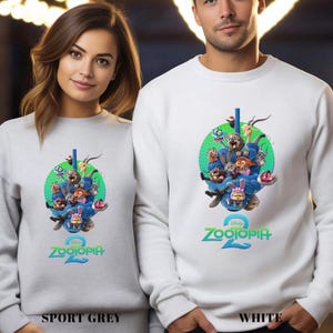 May include: Sport grey and white sweatshirts featuring a colorful graphic of characters from the Disney movie "Zootopia 2". The design includes a green circle with various animal characters and the movie title in teal.