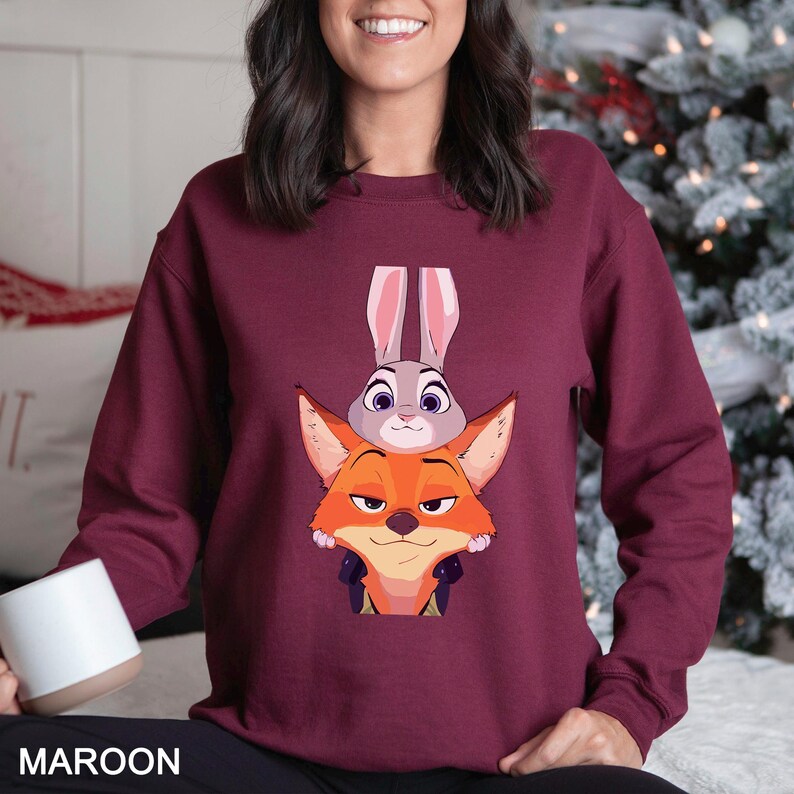 May include: Maroon sweatshirt featuring a cartoon image of a fox and a bunny. The fox is orange and the bunny is gray. The word "MAROON" is printed at the bottom of the sweatshirt.