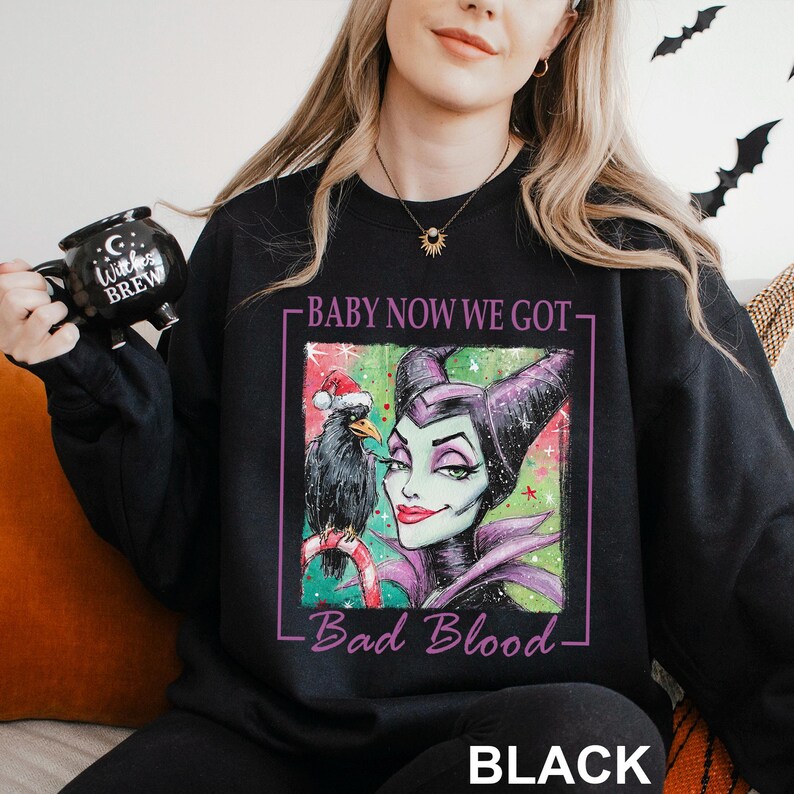 May include: Black sweatshirt featuring a graphic of a cartoon villain with a raven wearing a Santa hat. The text reads "BABY NOW WE GOT - Bad Blood - BLACK". The sweatshirt is a Halloween or holiday-themed item.