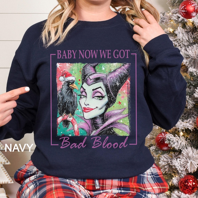 May include: Navy blue sweatshirt featuring a graphic of Maleficent with a raven wearing a Santa hat. The text reads "BABY NOW WE GOT - Bad Blood". The sweatshirt is a festive holiday design.