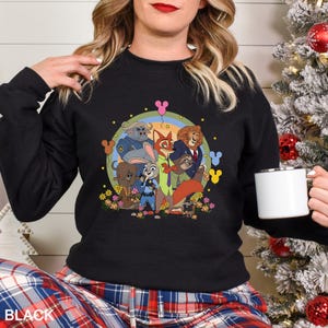 May include: Black crew neck sweatshirt with a vibrant Zootopia cartoon graphic. The design showcases Judy Hopps, Nick Wilde, and other characters in a circular arrangement with flowers and Mickey Mouse icons. The word "BLACK" is printed at the bottom of the sweatshirt.
