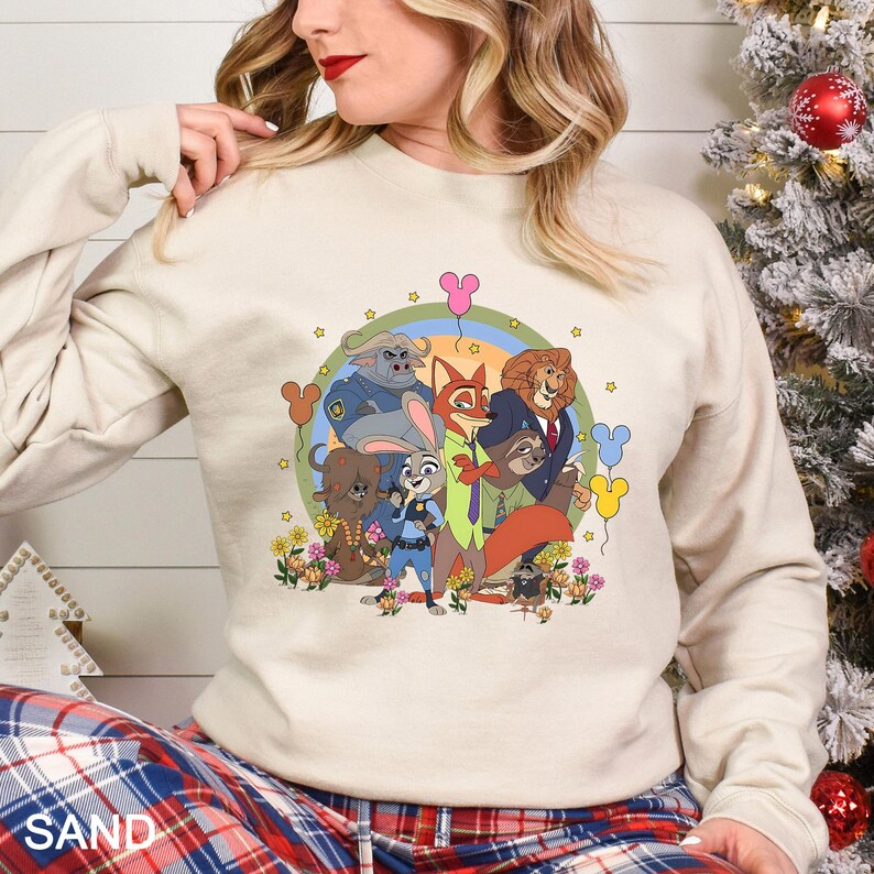 May include: A sand-coloured sweatshirt with a cartoon illustration of animal characters. The design includes a rainbow, flowers, and Mickey Mouse-shaped balloons. The word "SAND" is printed at the bottom left.