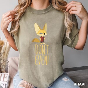 May include: Khaki-colored t-shirt featuring a cartoon fox with an angry expression. The fox is wearing a red shirt and black pants. The text "DON'T EVEN!" is printed in yellow below the fox.