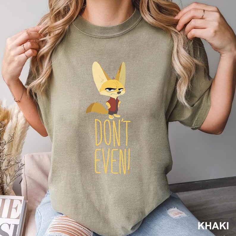 May include: Khaki-colored t-shirt featuring a cartoon fox with an angry expression. The fox is wearing a red shirt and black pants. The text "DON'T EVEN!" is printed in yellow below the fox.