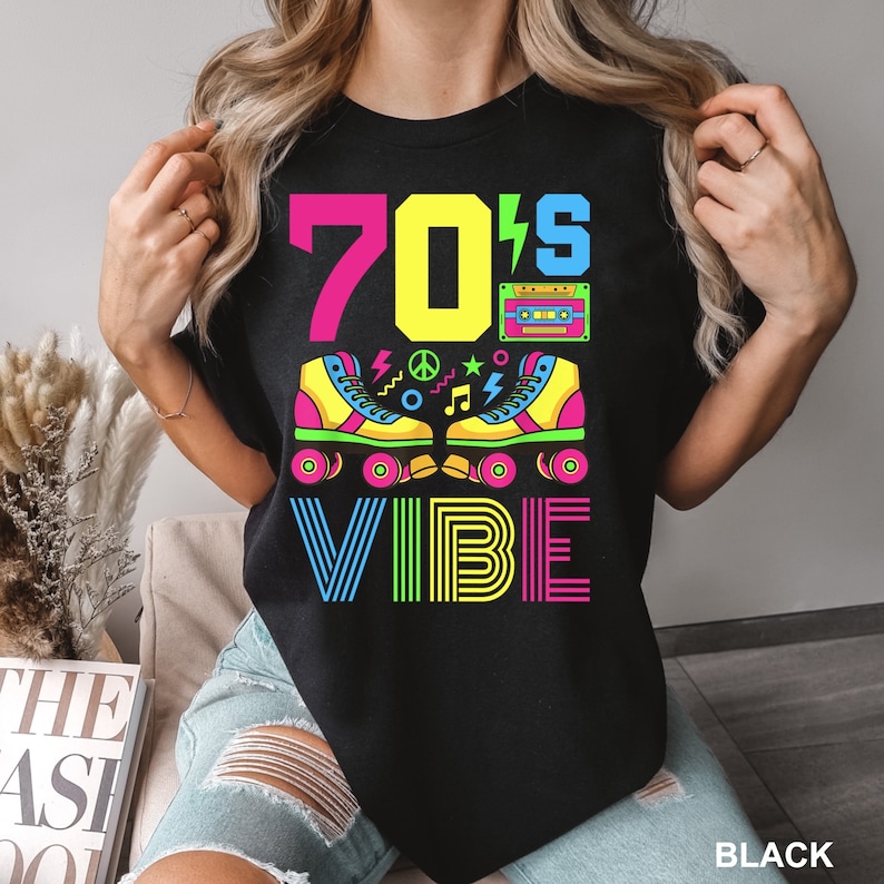 May include: Black t-shirt with a colorful graphic design featuring the text "70's VIBE" with roller skates, a cassette tape, and other retro symbols.