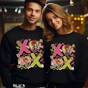 May include: Black sweatshirts featuring a Valentine's Day design with the characters Nick Wilde and Judy Hopps from Zootopia. The design includes pink and green XOXO letters, hearts, and cupcakes. The word "BLACK" is printed at the bottom.