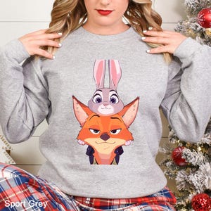 May include: A light gray sweatshirt featuring a cartoon image of a fox and a rabbit. The fox is orange with a sly expression, and the rabbit is gray with long pink ears. The text "Sport Grey" is at the bottom.
