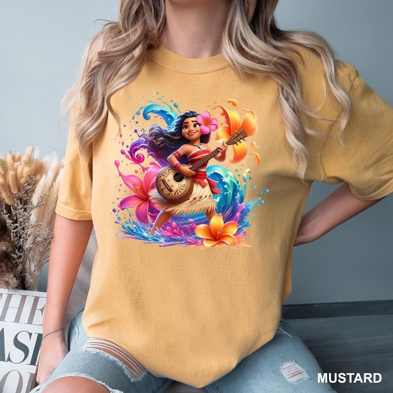 Puede incluir: Camiseta color mostaza con una ilustraci&oacute;n vibrante de un personaje de dibujos animados tocando el ukelele, rodeado de flores y salpicaduras de agua coloridas. El personaje lleva una flor en el pelo y una falda tradicional.