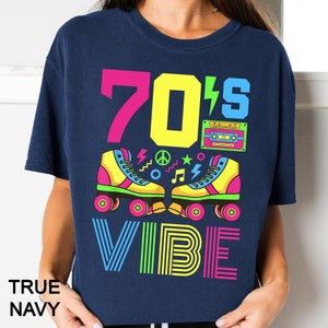 May include: A navy blue t-shirt with a graphic design featuring the text "70's Vibe" in neon colors. The graphic also includes a pair of roller skates, a cassette tape, and peace signs.