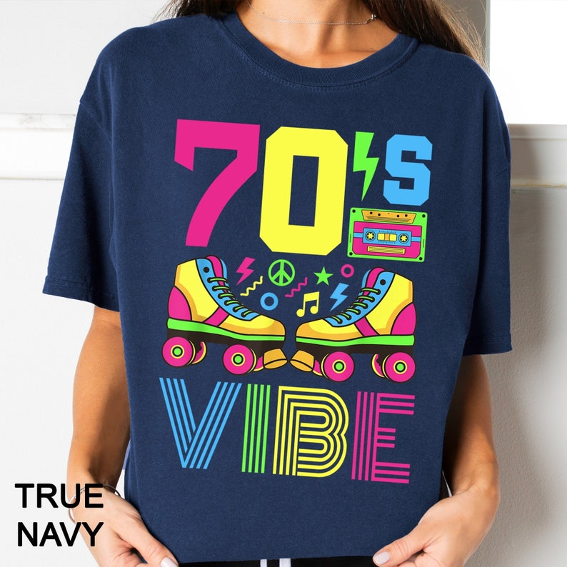 May include: A navy blue t-shirt with a graphic design featuring the text "70's Vibe" in neon colors. The graphic also includes a pair of roller skates, a cassette tape, and peace signs.