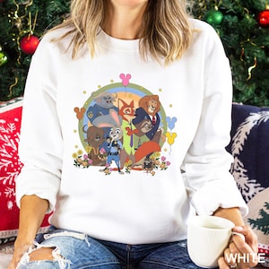 May include: White crew neck sweatshirt with a colourful graphic of animated animal characters. The design includes a rainbow, flowers, and Mickey Mouse-shaped balloons. The characters are arranged in a circle, creating a cheerful design.