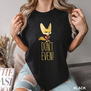 May include: Black t-shirt featuring a cartoon fox with large ears and a stern expression, wearing a red vest. The text "DON'T EVEN!" is printed in yellow below the fox. The word "BLACK" is printed at the bottom right.