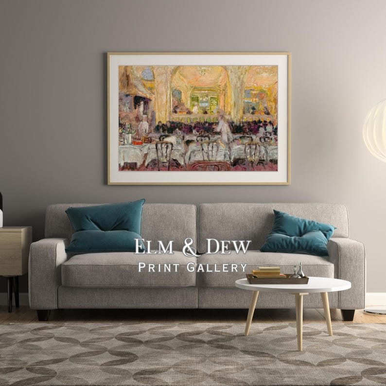 May include: A framed print of a restaurant scene hangs above a gray sofa with teal pillows. The print features a colorful impressionistic painting of a dining room with tables and chairs. The text "ELM & DEW PRINT GALLERY" is below the sofa.