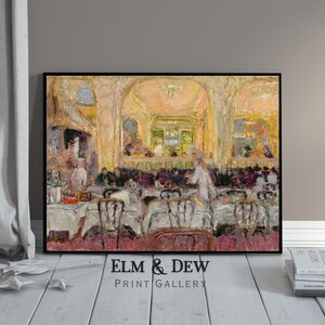 May include: A framed print of an impressionist painting depicting a restaurant scene. The artwork features tables with white tablecloths, chairs, and figures in the background. The color palette includes warm tones of yellow, beige, and hints of purple. The text "ELM & DEW PRINT GALLERY" is at the bottom.