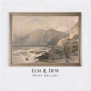 Puede incluir: Una impresión enmarcada de un paisaje con una cordillera, una cascada y una masa de agua. La obra de arte está en tonos apagados de gris, beige y marrón. El marco es de color oro claro. El texto "ELM & DEW PRINT GALLERY" está en la parte inferior.